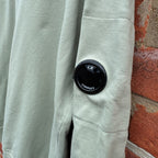 C.P. Company green sweatshirt with ribbed hem and signature goggle lens detail.
