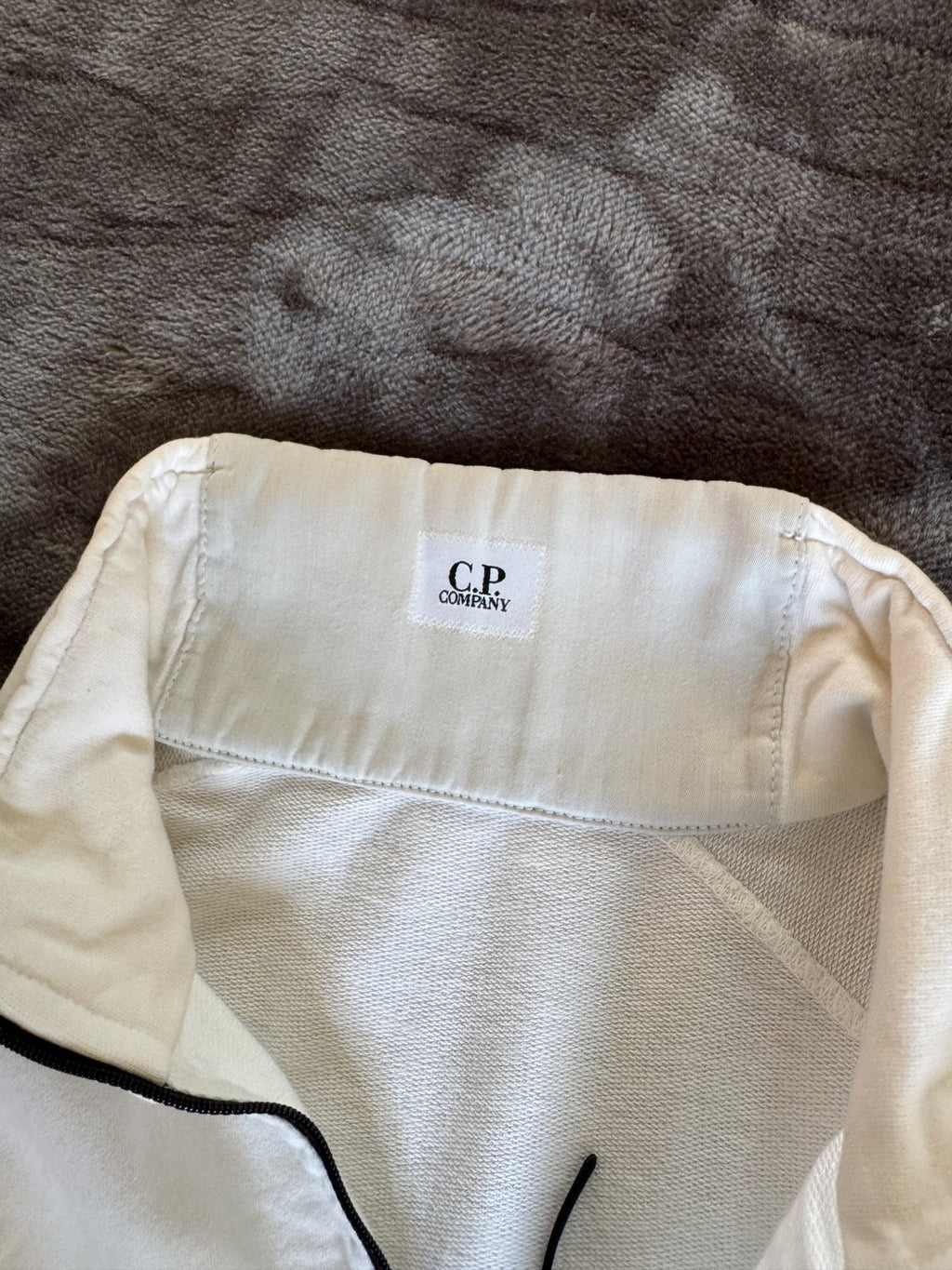C.P. Company white quarter zip sweatshirt with logo patch and soft cotton material.