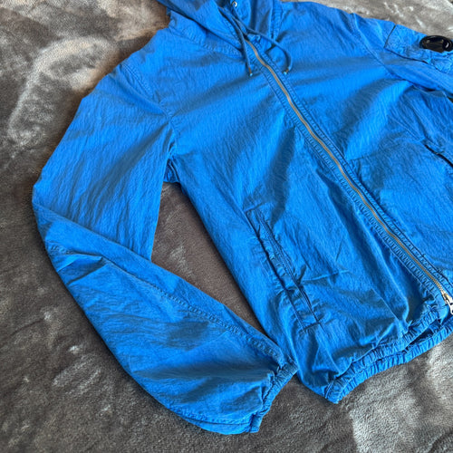 C.P. Company blue windbreaker jacket with big lens detail and garment-dyed finish.