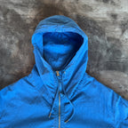 C.P. Company blue windbreaker jacket with big lens detail and garment-dyed finish.