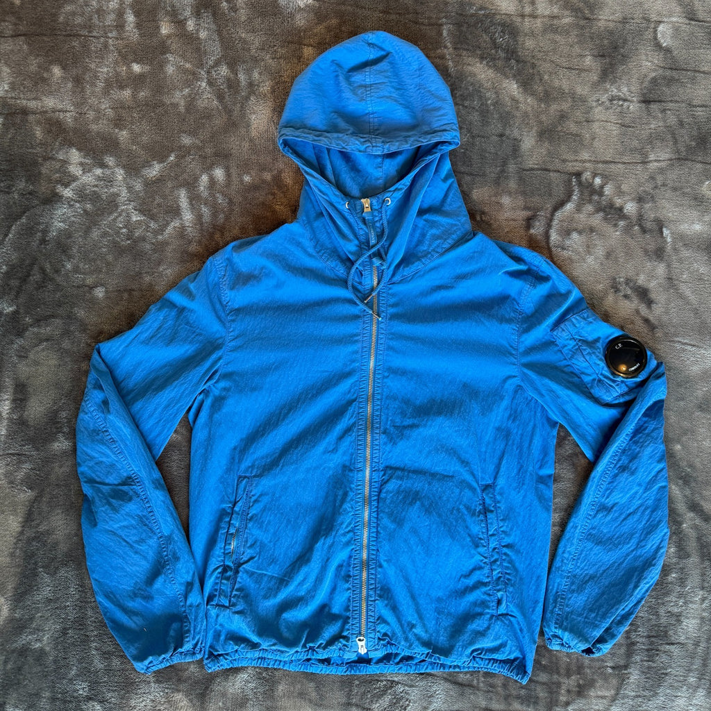 C.P. Company blue windbreaker jacket with big lens detail and garment-dyed finish.