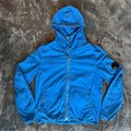 C.P. Company blue windbreaker jacket with big lens detail and garment-dyed finish.