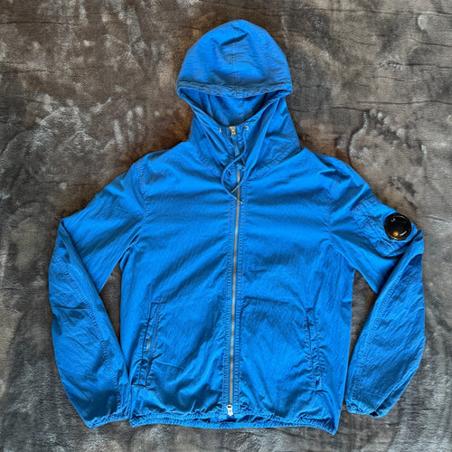 C.P. Company blue windbreaker jacket with big lens detail and garment-dyed finish.