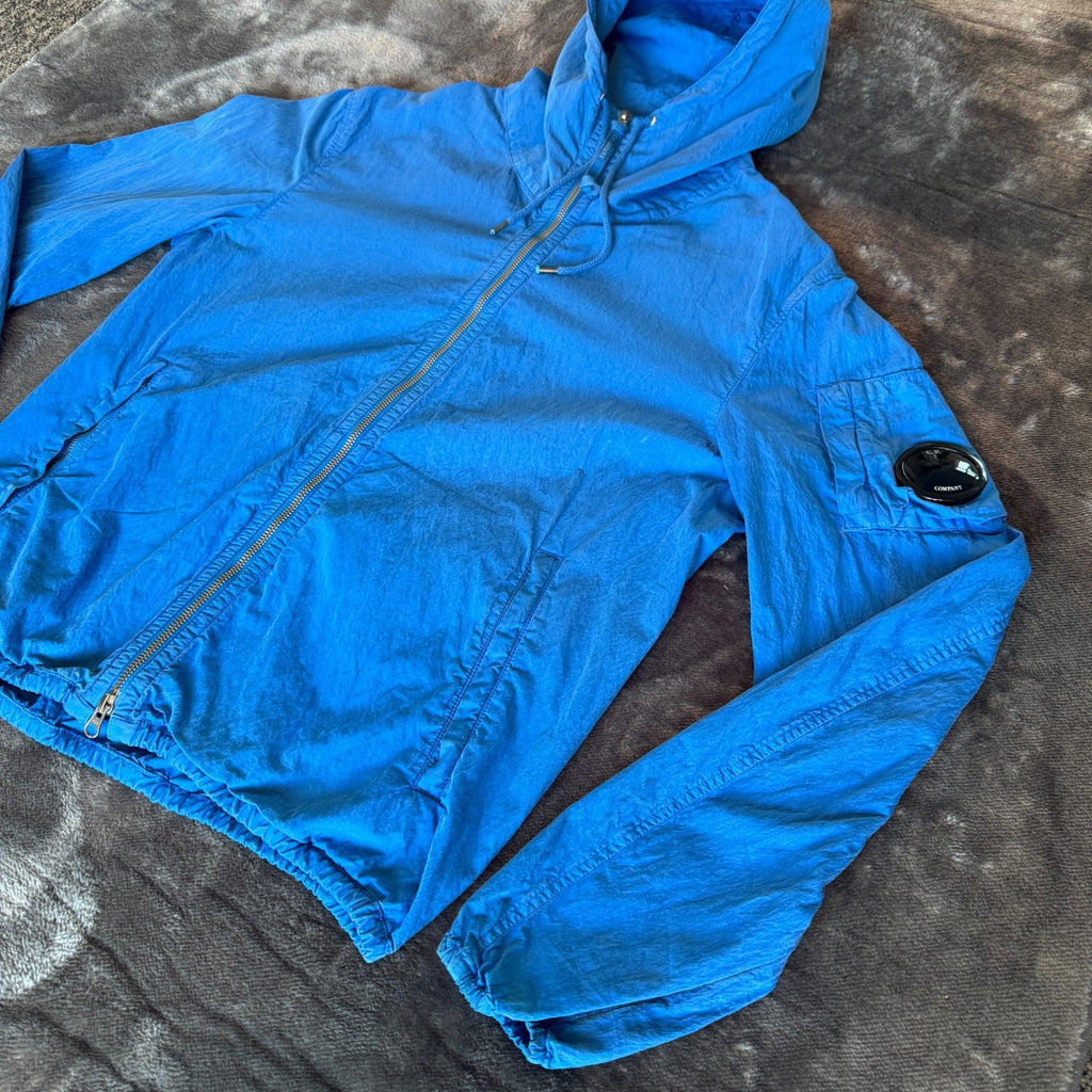 C.P. Company blue windbreaker jacket with big lens detail and garment-dyed finish.